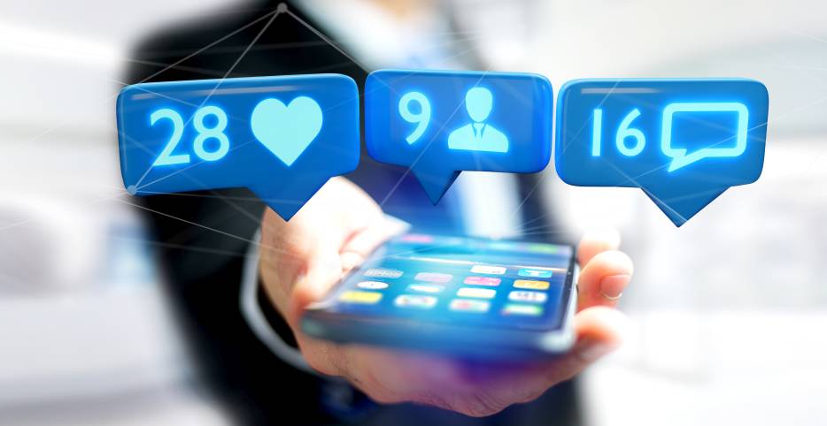 Man in suit holding a cellphone that has social media notification icons on it